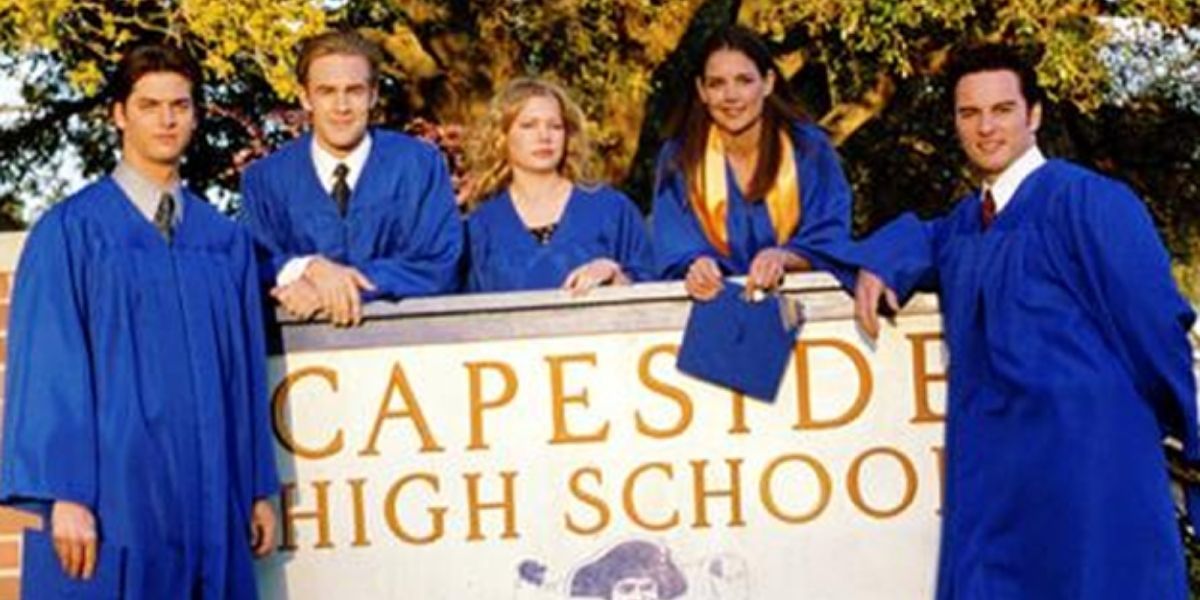 The cast of Dawson's Creek posing in their caps and gowns in front of the school sign