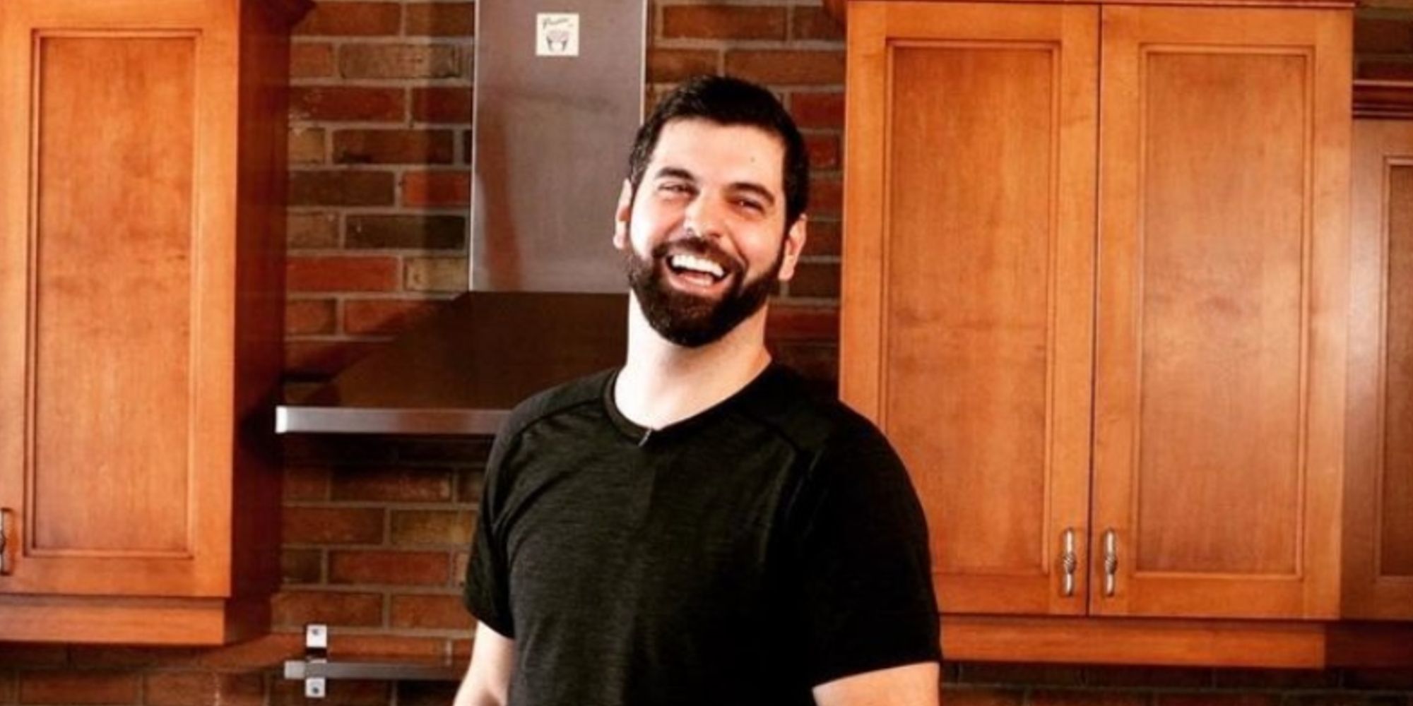 Chef Matt Burns from Below Deck in black tee shirt, laughing, standing in a kitchen