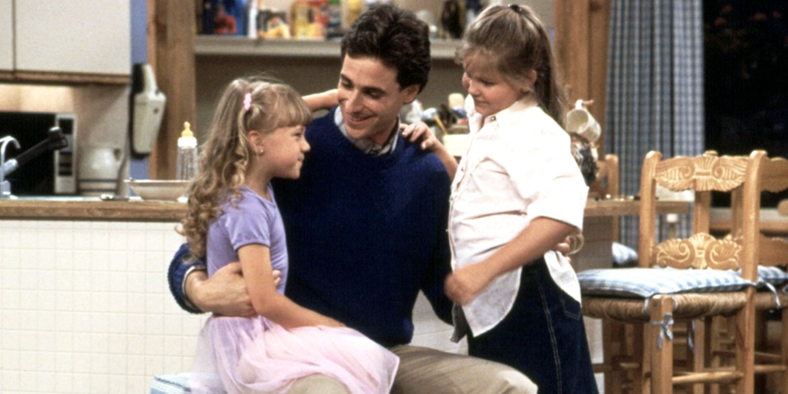 Danny Tanner abraçando suas filhas Stephanie e DJ na cozinha em Full House