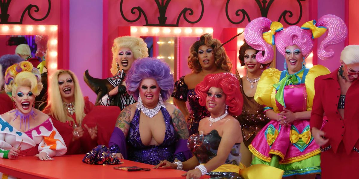 A cast photo of 9 drag queens gathered around a table in RuPaul's Drag Race Down Under.