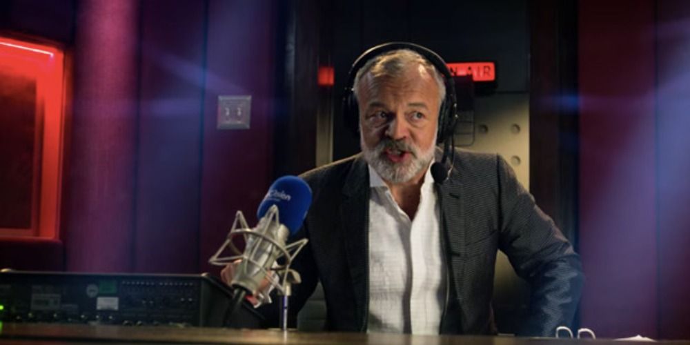 Graham Norton in Eurovision Song Contest The Story of Fire Saga as a commentator in front of a microphone, wearing headphones