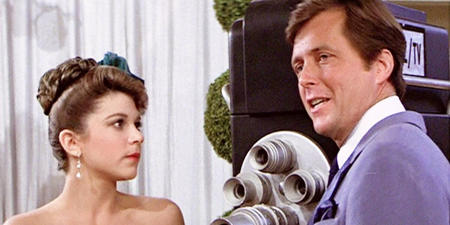 Vince Fontaine talks to Marty in front of a camera at the dance in Grease