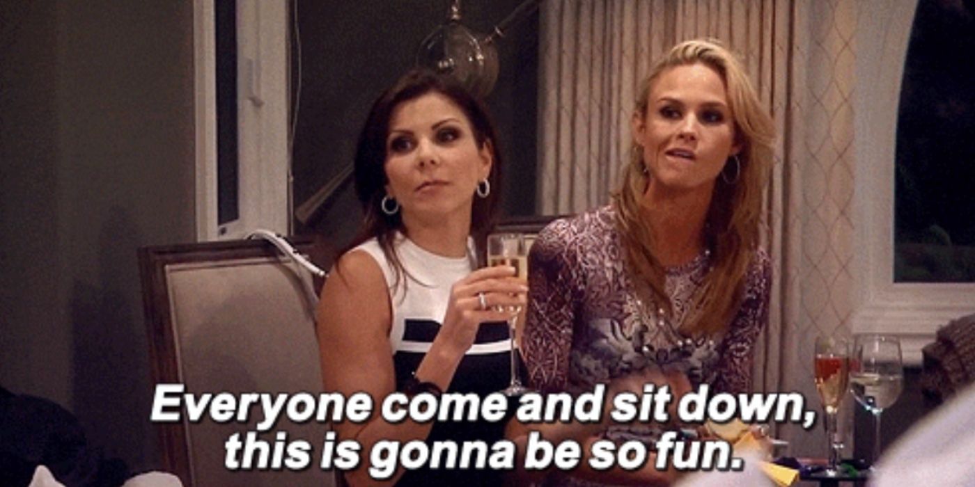 Heather and Meghan sitting at a table while trying to get the orther ladies to sit on RHOC