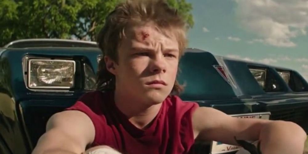 Henry Bowers dans Ça Chapitre 1, assis devant un camion, vêtu d'une chemise sans manches rouge