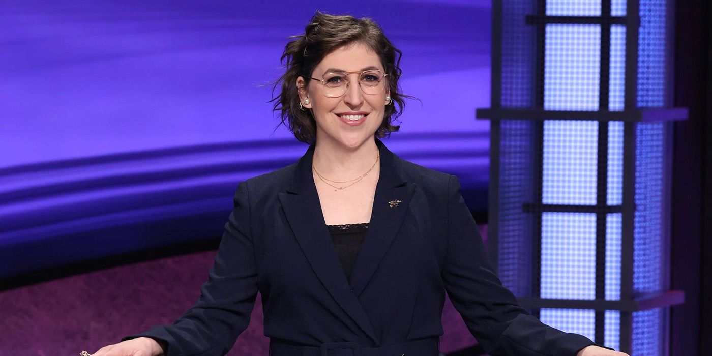 Mayim Bialik standing behind a podium on Jeopardy as host