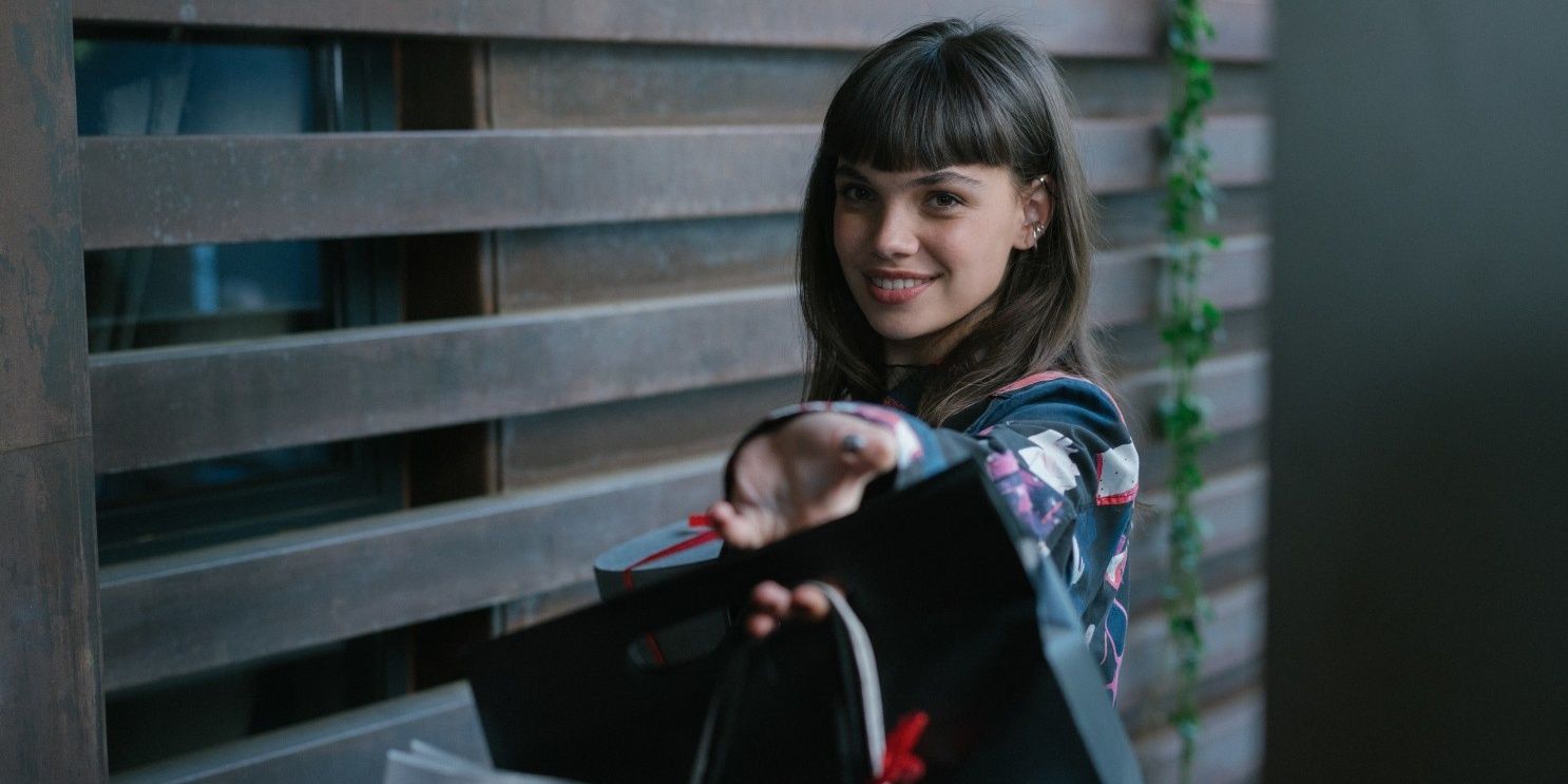 Mencia smile and holds out shopping bags in a doorway in Élite