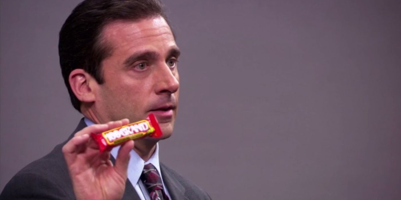 Michael Scott holding a candy bar in front of a lecture hall on The Office.