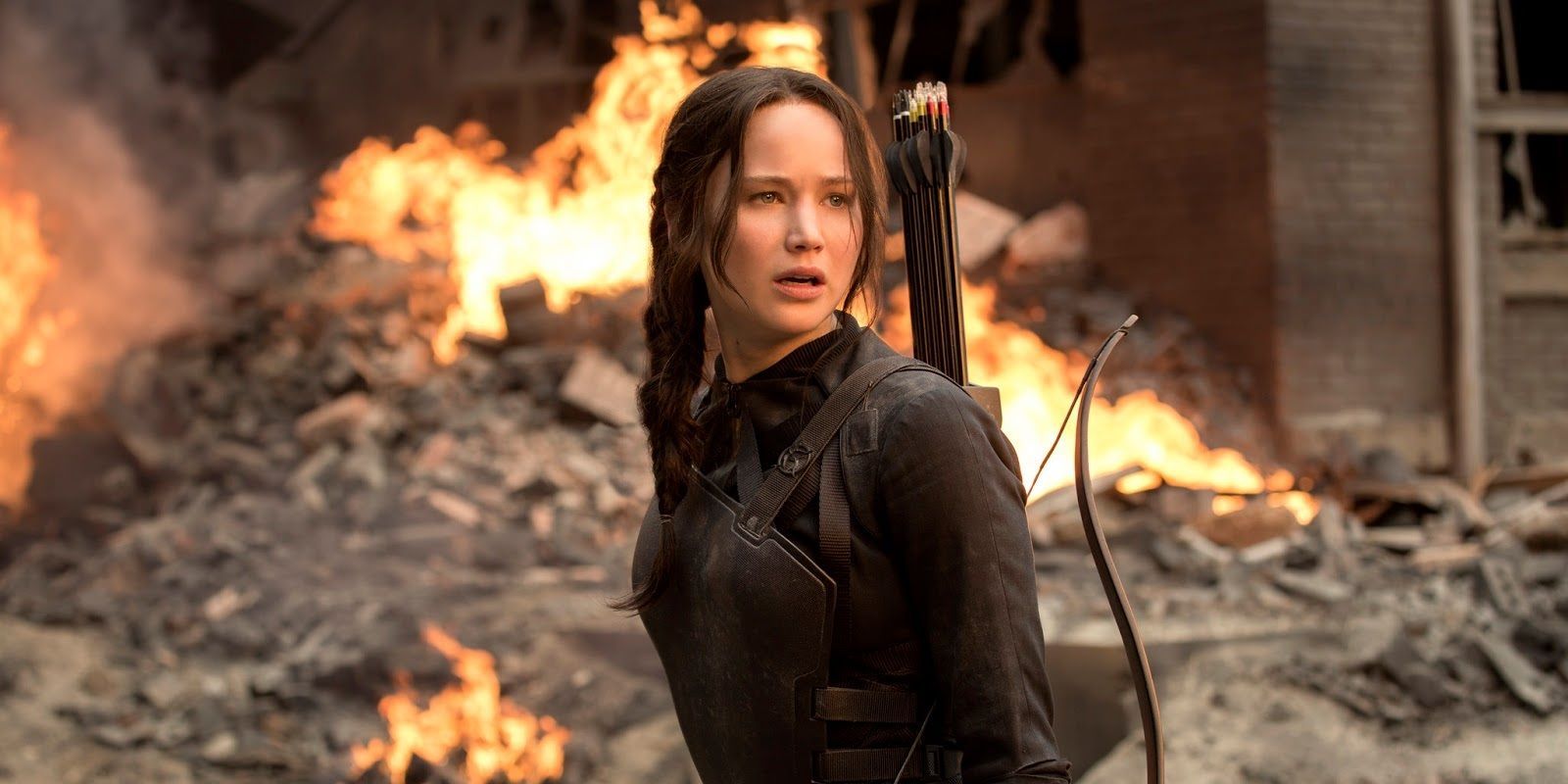 Katniss na frente de um fundo flamejante em Jogos Vorazes.