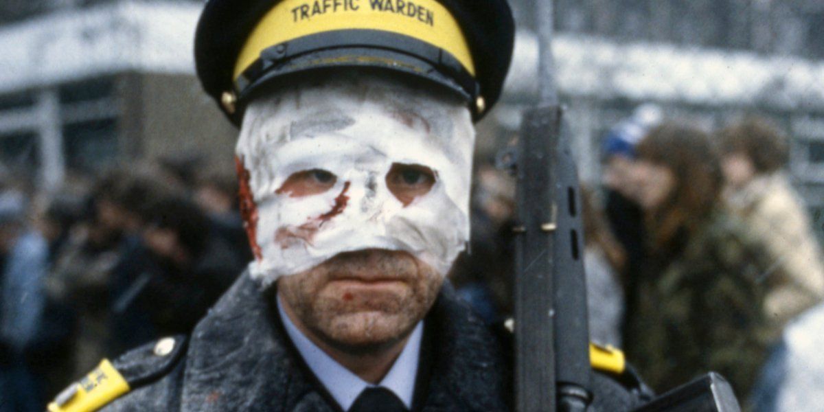 A traffic warden with a gun on his shoulder and his face covered in Threads