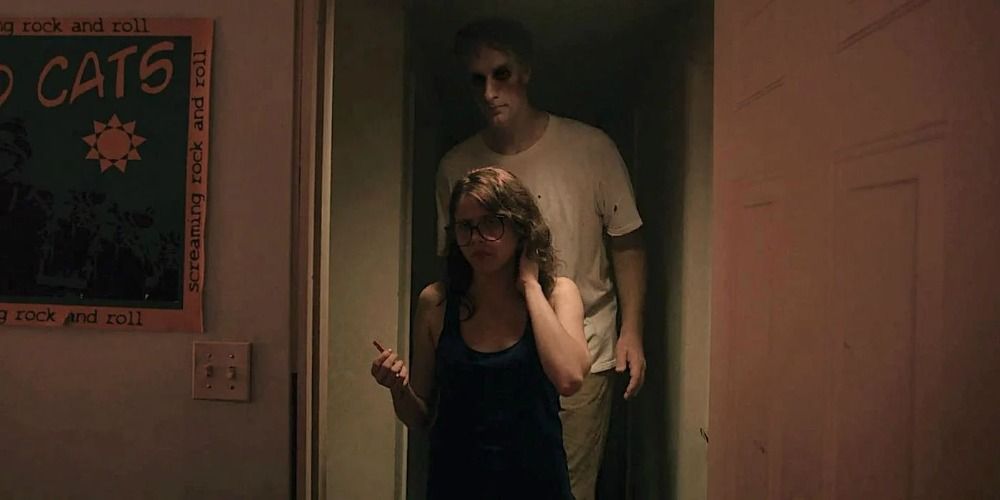a girl in It Follows walks through a doorway, oblivious to the tall menacing man behind her
