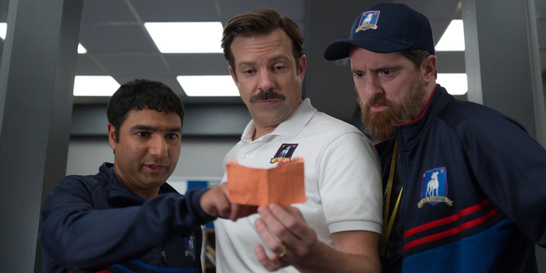 Ted, Nate and Coach Beard looking at a note in Ted Lasso