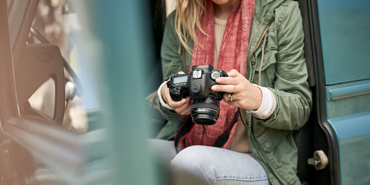 A woman holding a digital camera with a Tile Sticker on its top.
