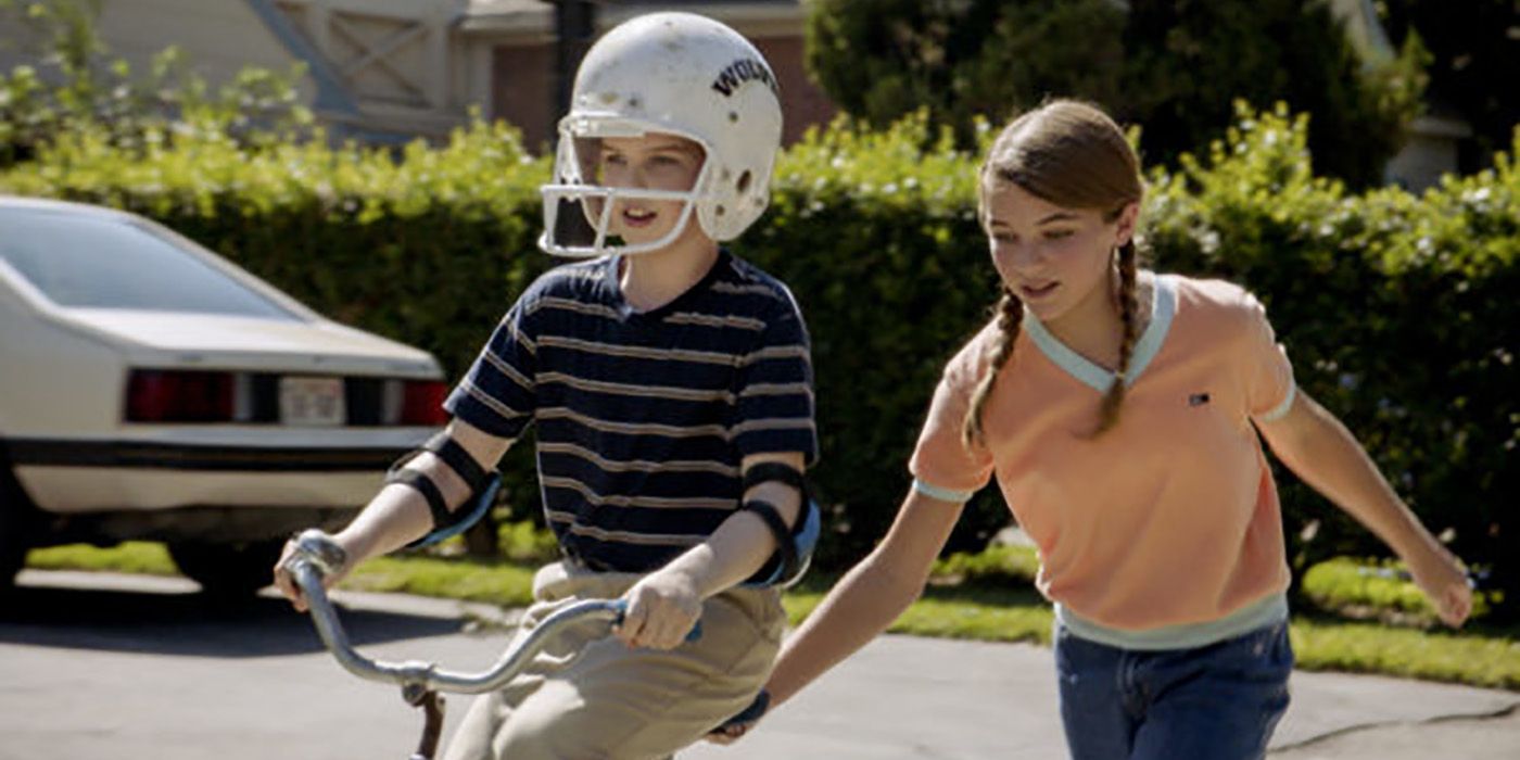 Sheldon riding a bike wearing a helmet, Missy holding it from behind on Young Sheldon.