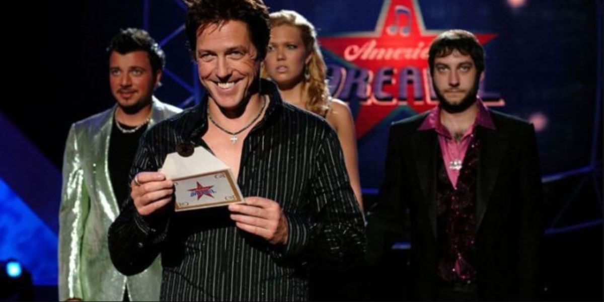 Hugh Grant holding an envelope with show winner as Mandy Moore and other contestants stand nervously behind him in American Dreamz