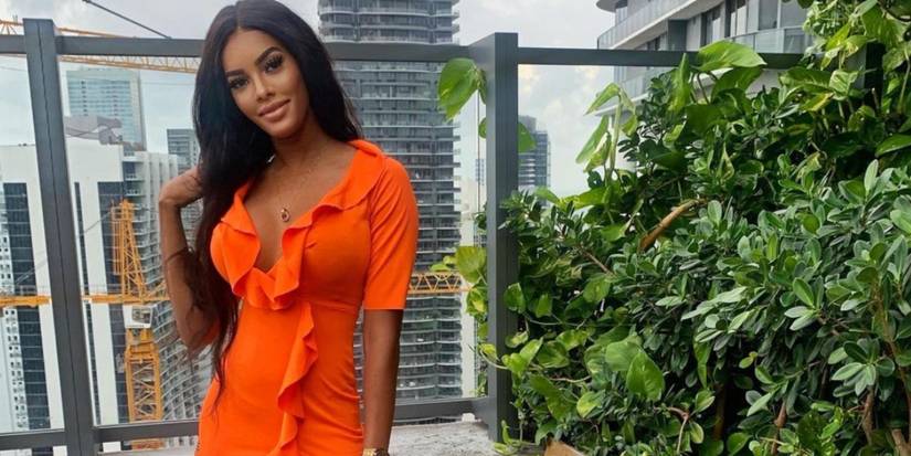 Below Deck's Lexi Wilson wears an orange dress and looks dolled-up in makeup with long hair.