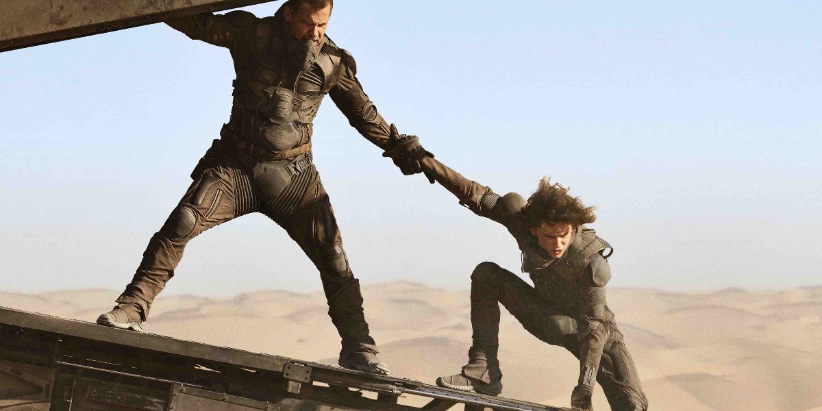 Gurney holding Paul's hand as they fly over the desert in Dune (2021).