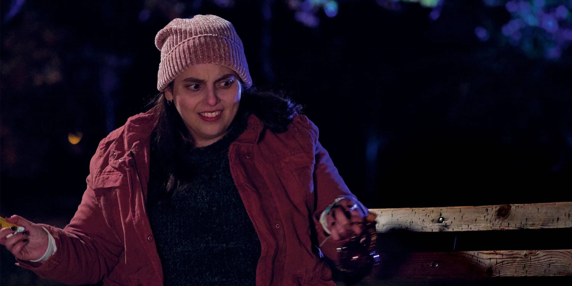Jenna sits outside in a pink jacket in What We Do in the Shadows.