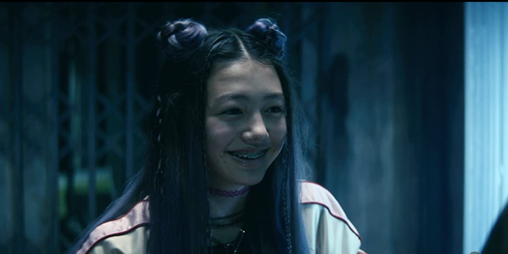 An image of Ani smiling and exposing her braces in the movie Kate.