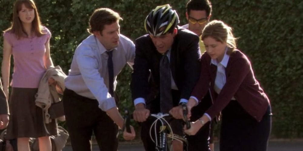 Michael from The Office riding a bike in the parking lot, supported by Jim and Pam