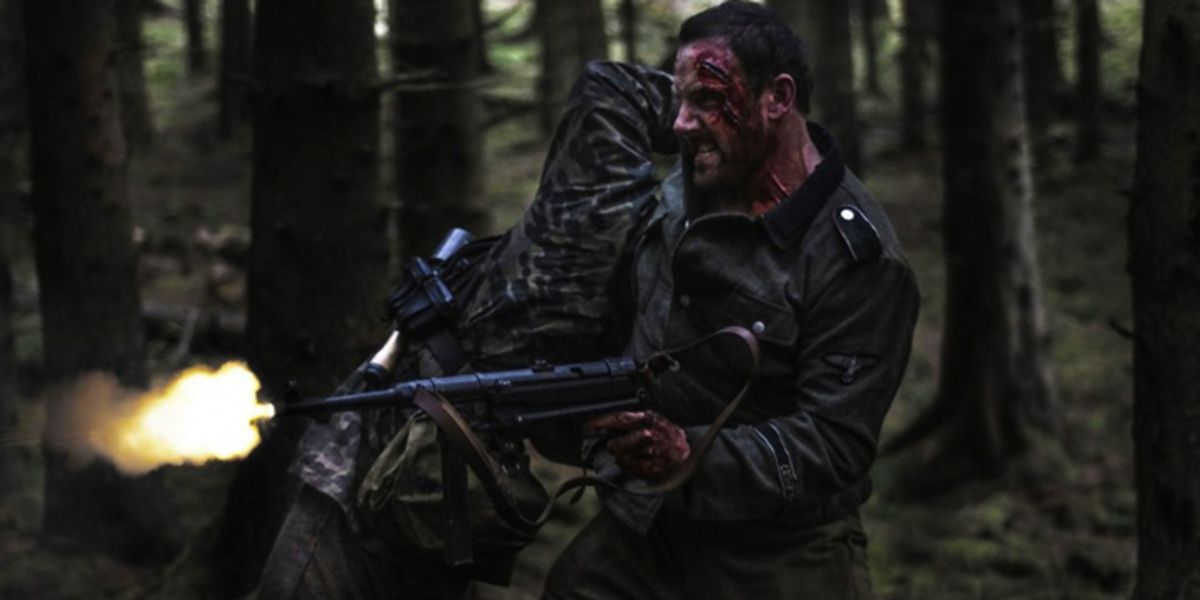 DC (Rey Stevenson) shooting at zombies attacking in the woods in Outpost