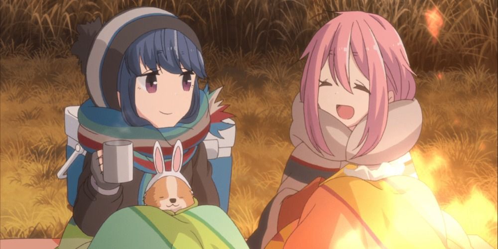 Rin and Nadeshiko of Laid Back Camp sitting by a campfire, bundled up in blankets and smiling