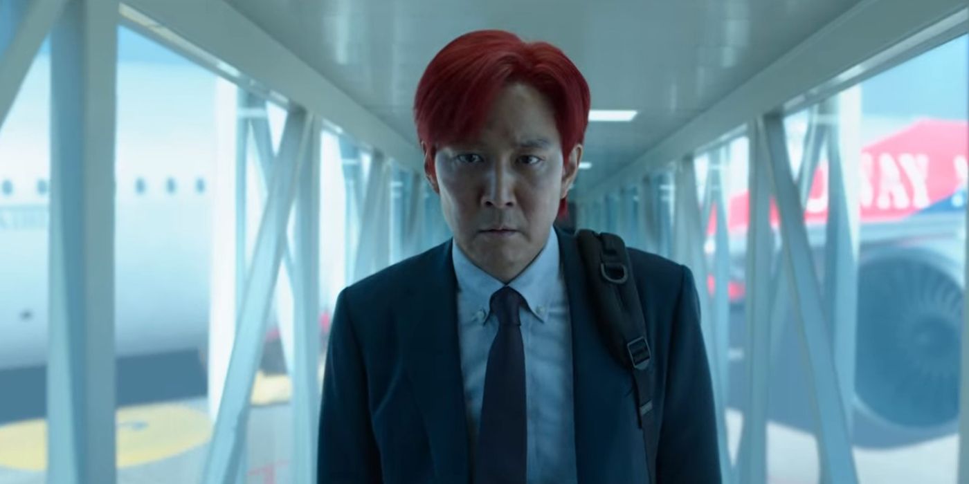 Gi-hun, with his hair dyed red and in a business suit, walks down an airport hallway in Squid Game.