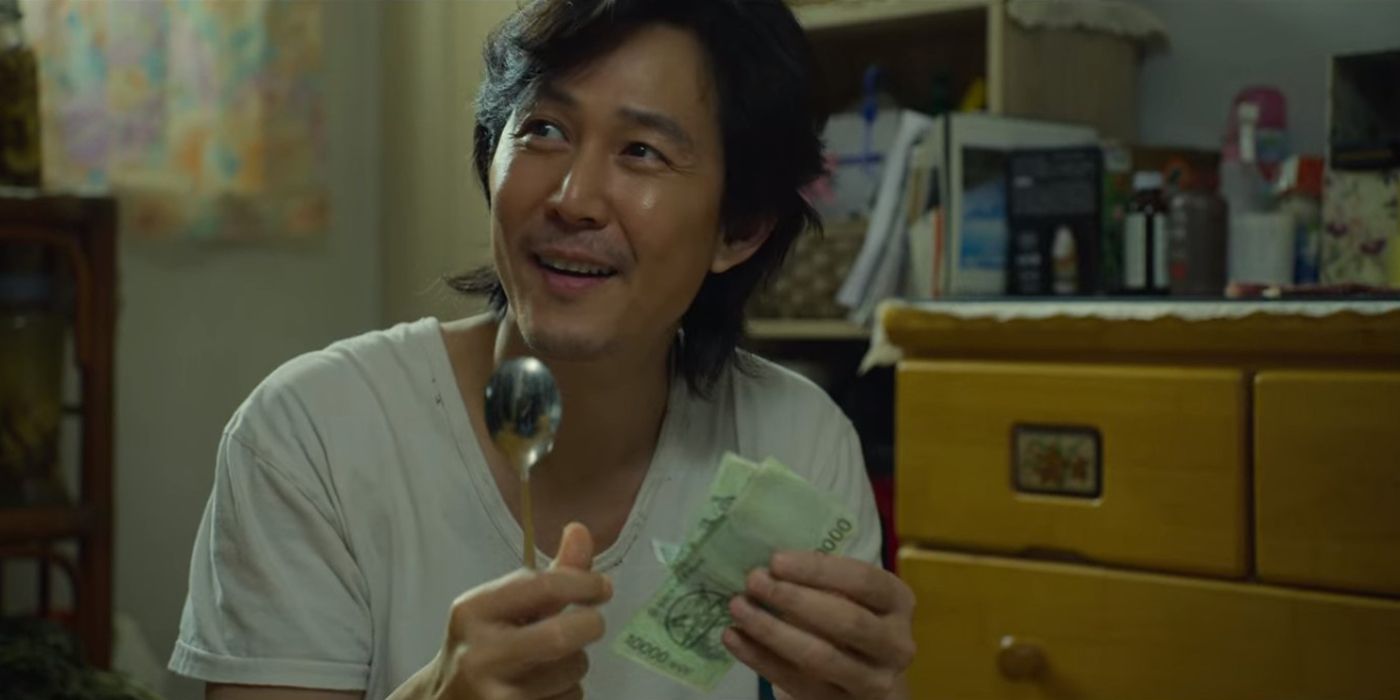 Seong Gi-Hun smiles while holding a spoon and some money in Squid Game