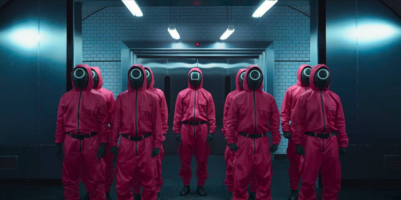 Nine men stand in pink jumpsuits and black masks in a dimly lit room in Squid Game.