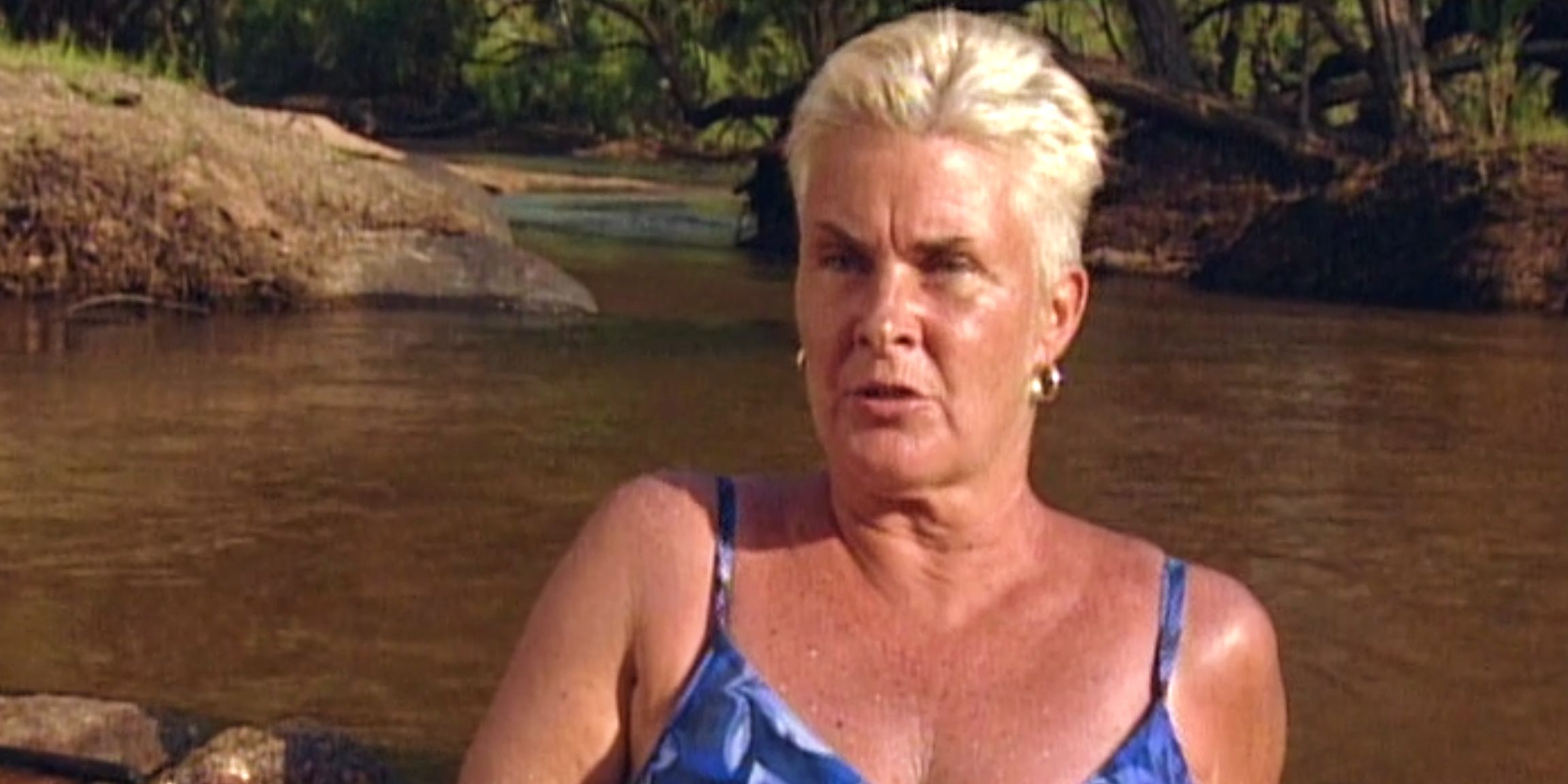 Mad Dog wears a bathing suit and sits in a stream while giving a confessional interview on Survivor