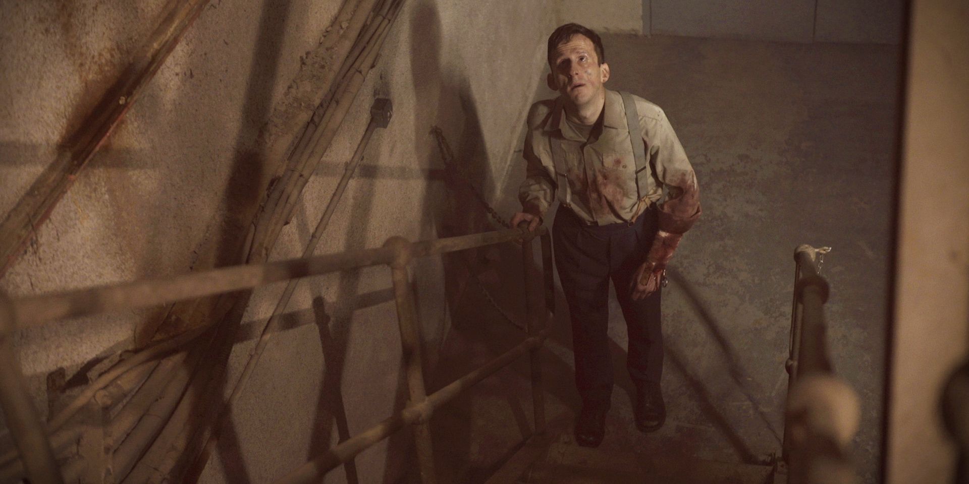 A bleeding man looks up at some stairs in The Bunker.