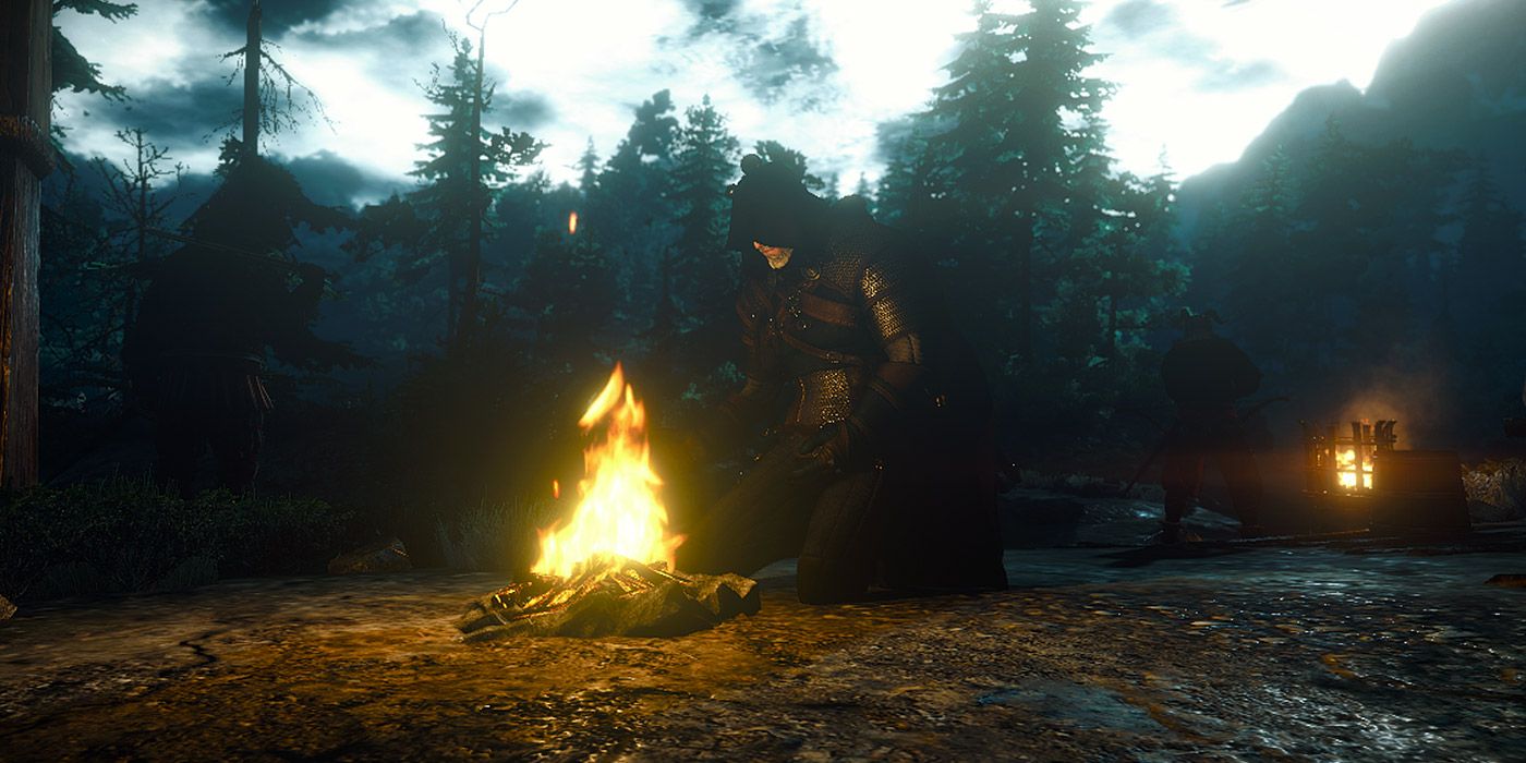 A cloaked Geralt kneeling in front of a campfire in The Witcher III