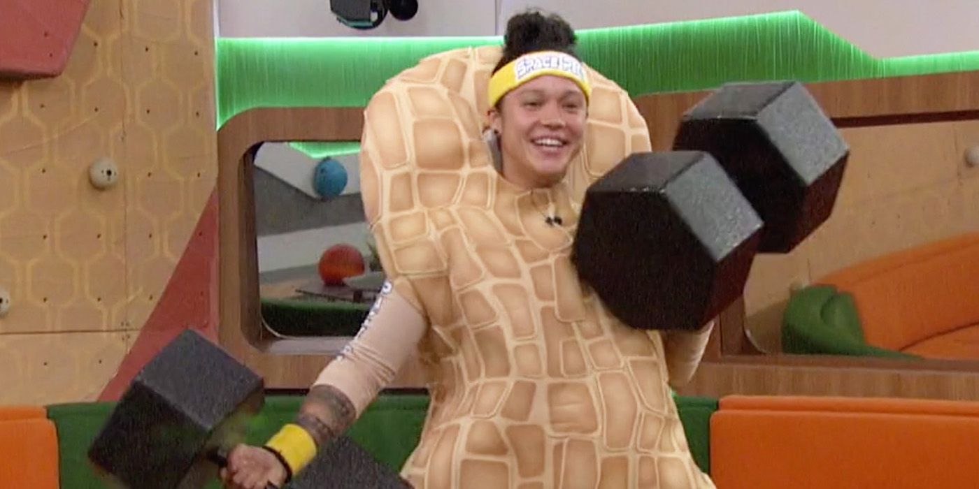 Kaycee dressed as a peanut on Big Brother, holding oversized dumbbells.