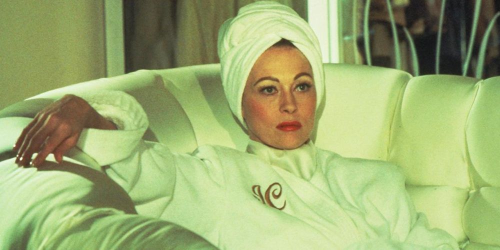 Joan sits on a sofa wearing a monogram robe in Mommie Dearest