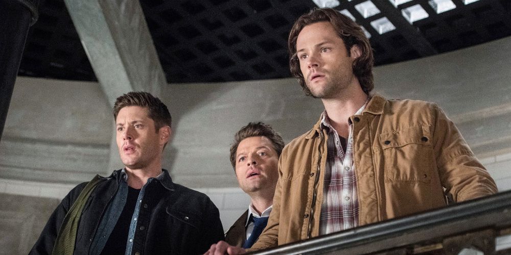 Dean, Castiel, and Sam look down from a balcony on Supernatural