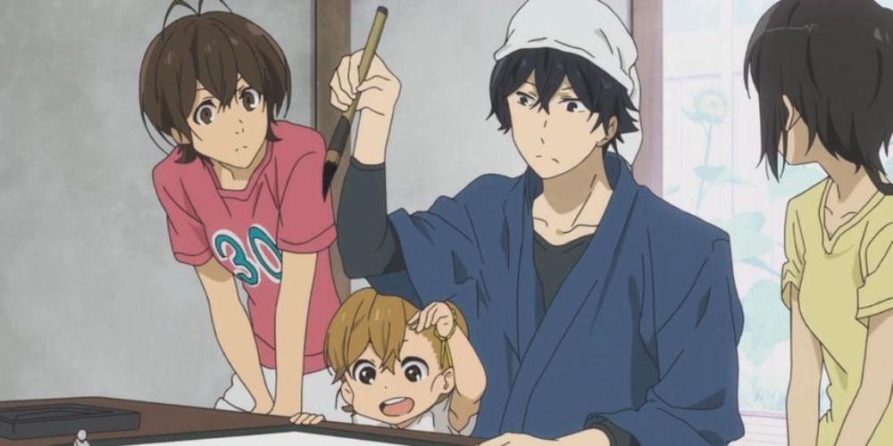 o personagem principal de Barakamon segurando um pincel de caligrafia enquanto uma garotinha está sentada em seu colo, outras duas garotas estão ao seu lado