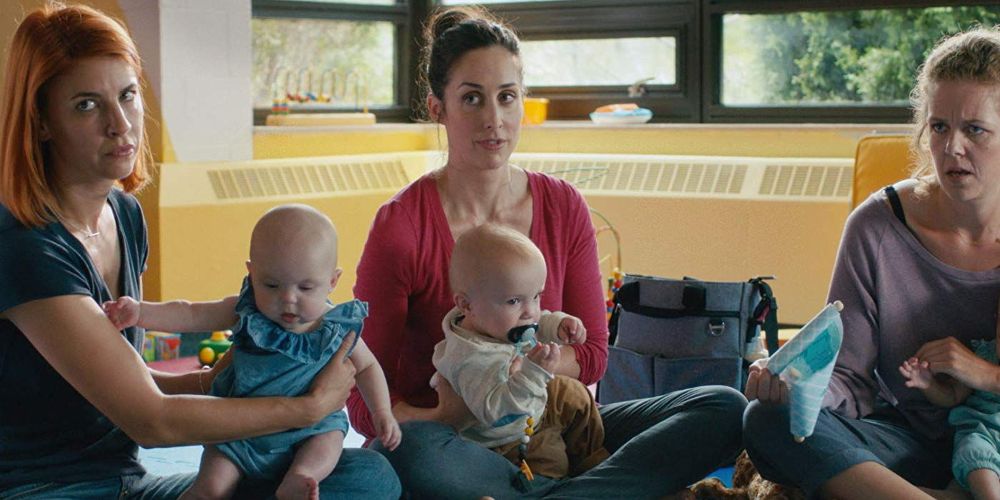 Kate holds her baby while sitting on the floor in Workin' Moms