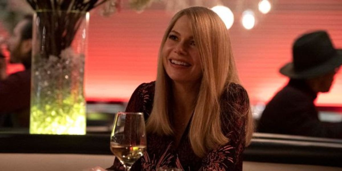 Anne Weying in Venom 2, smiling at a dinner table with a glass of wine beside her.