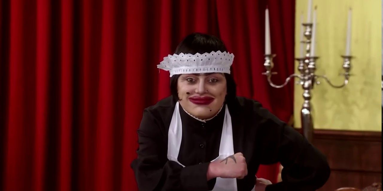 Baga Chipz dressed as a maid mugs for the camera in Drag Race UK.