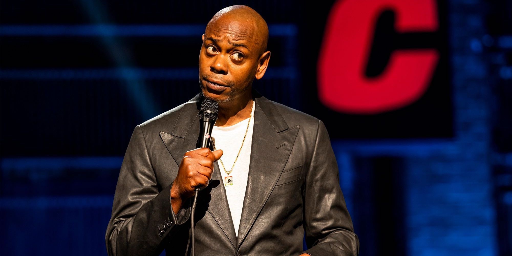 Dave Chappelle standing on stage and holding a mic.