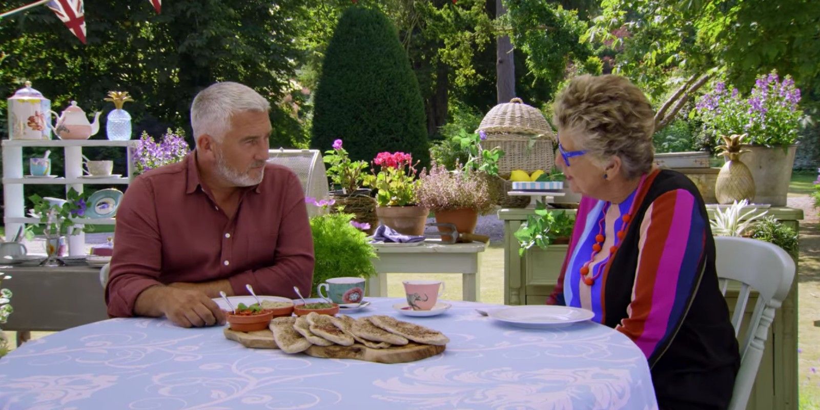 Paul Hollywood and Pru Leith talk at a table in The Great British Bake Off