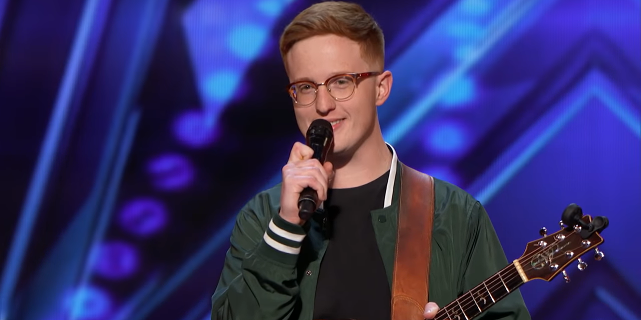 Lamont Landers in a green jacket with a guitar, smiling on he stage of AGT