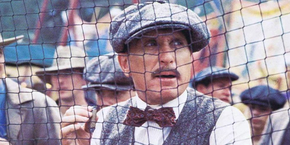Robert Duvall in The Natural in a cap and bow tie as he stares through a wire fence.