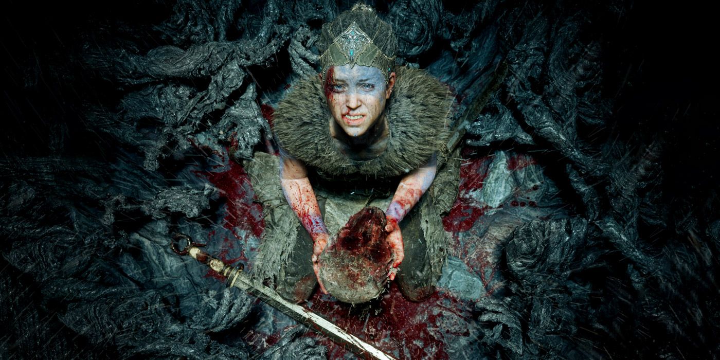 Senua looking up at the camera on her knees in Hellblade, holding a severed head.