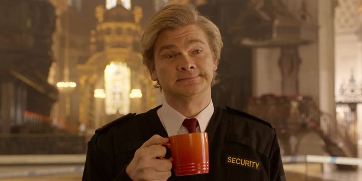 Simon Farnaby in Paddington 2, in a security uniform holding a mug of coffee