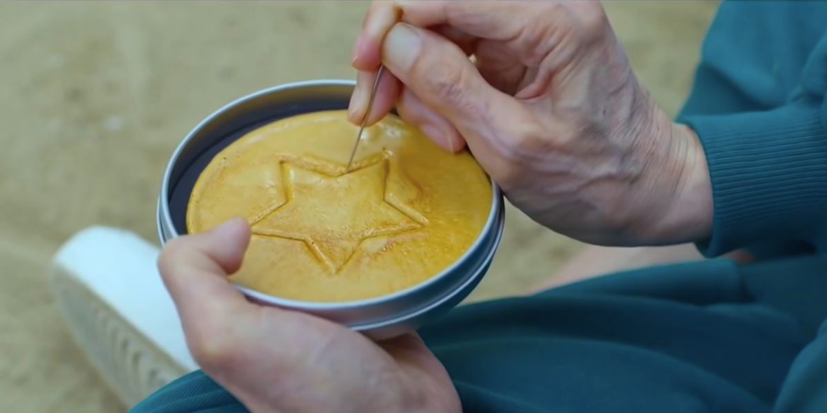 A contestant cutting out a star shape from a dalgona cake during the game in Squid Game