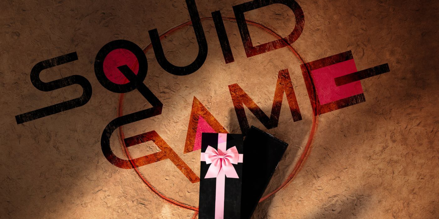 An overhead shot of black coffin with a pink ribbon on the ground with the show's title, Squid Game, written on top of a circle on the floor..