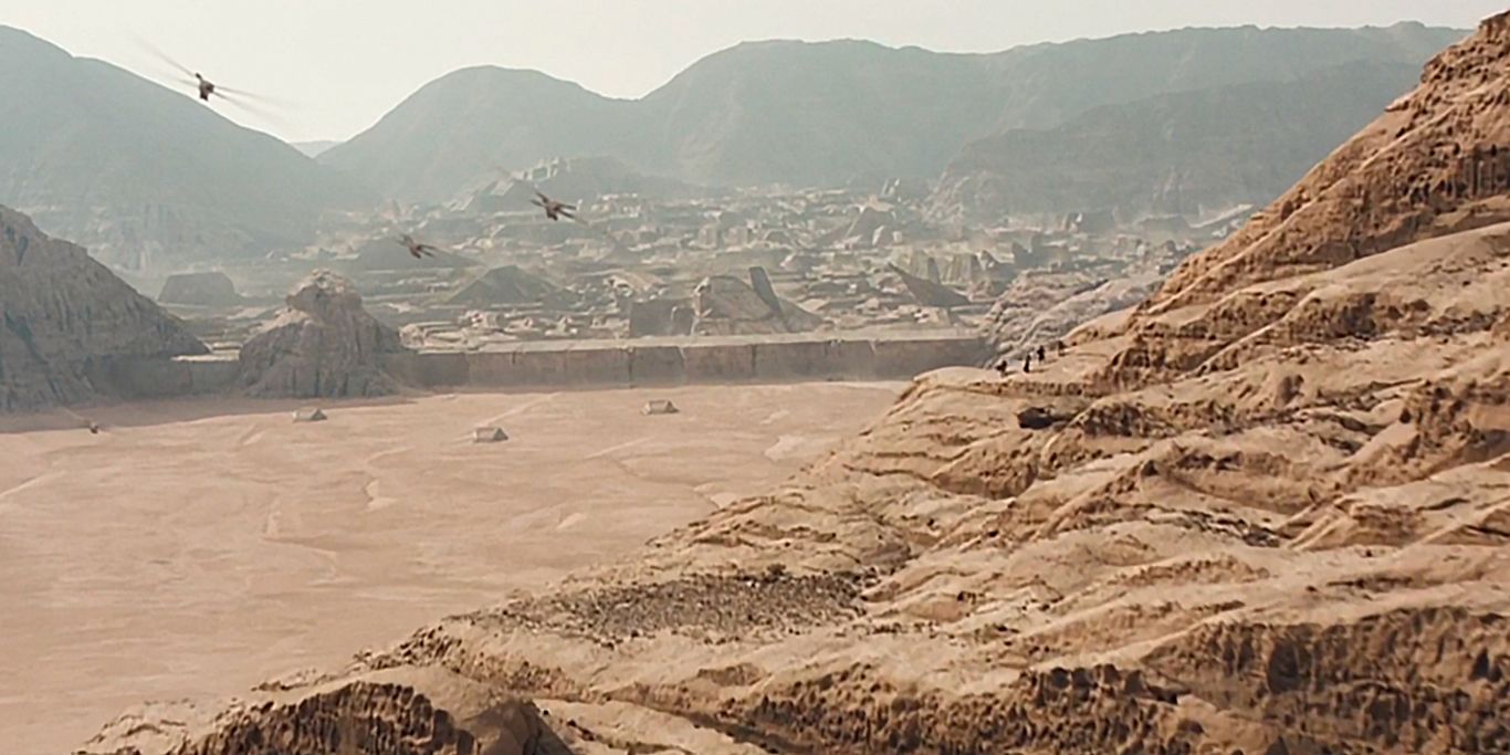 Thopters fly over a mountain and towards the Arrakeen capital city in Dune (2021).