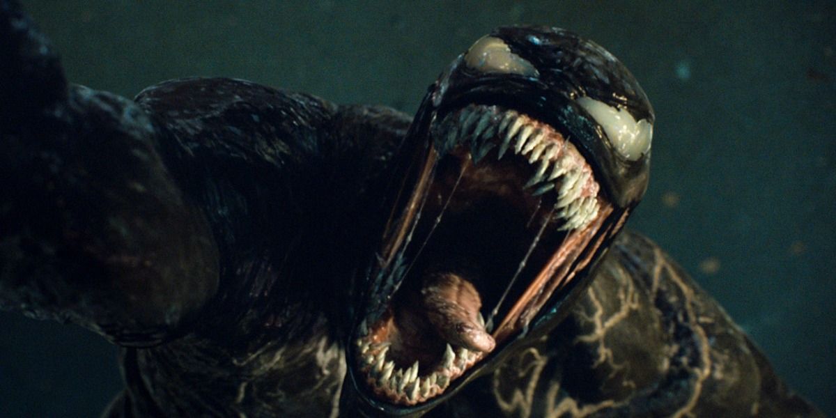 Venom in Venom 2, holding someone in the air, opening his mouth really wide to show off his teeth