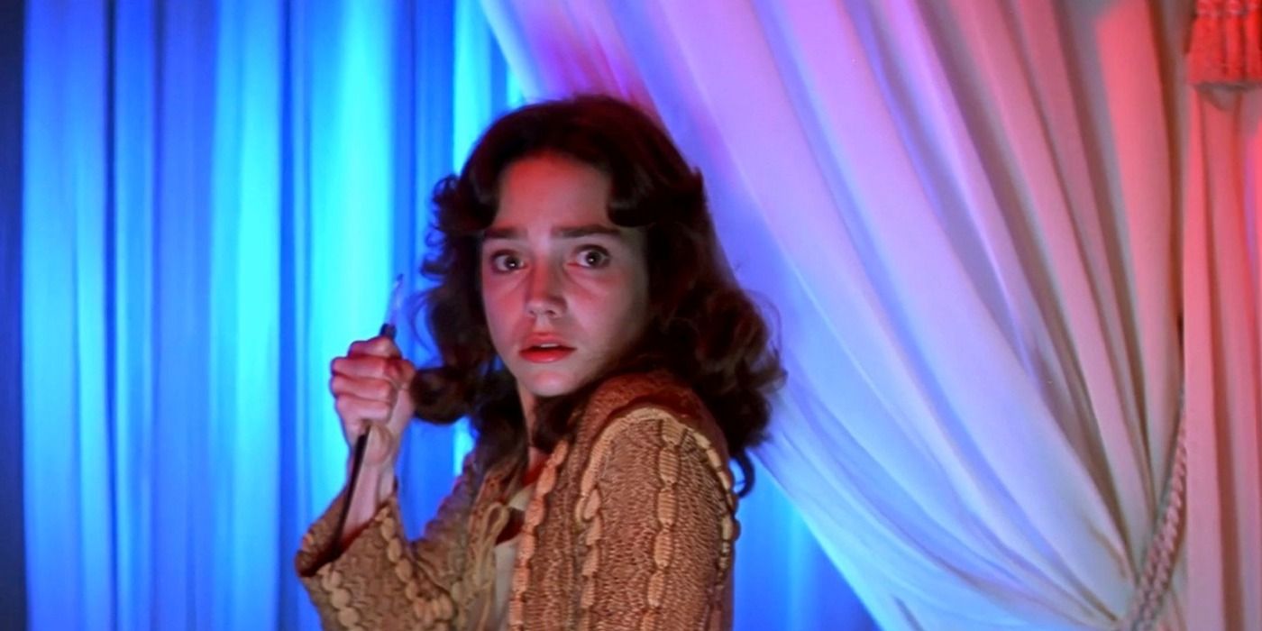 Woman holding a knife in front of a curtain in Suspiria.
