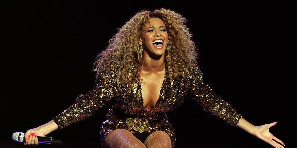 Beyonce leans forward on stage while wearing a gold bedazzled dress